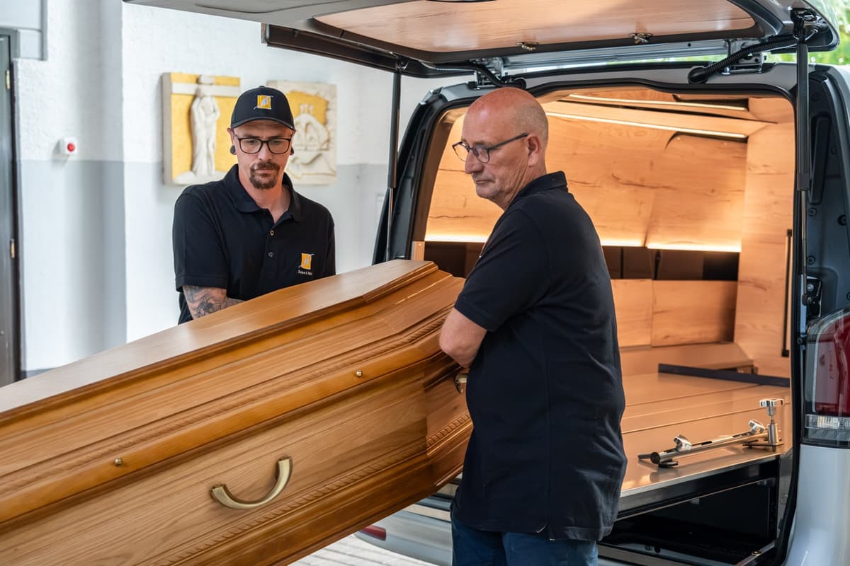 Das Team von Dahm & Fils lädt einen Sarg in den Bestattungswagen